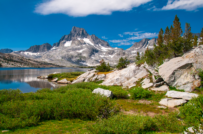 a rocky river with trees on the side of a snow covered mountain